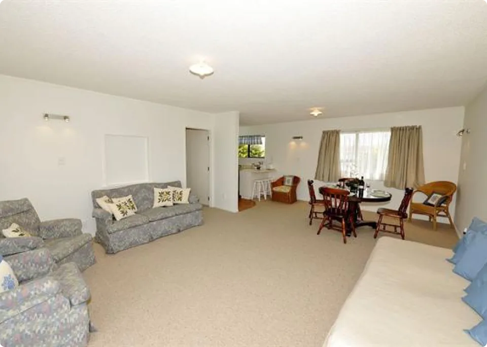 A spacious living room with a sofa and table set, allowing the whole family to relax in a bright, sunny space. Natural light from the windows creates a cozy atmosphere.